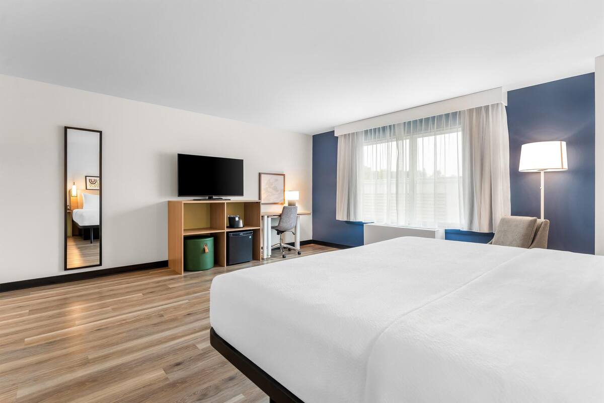 Quarto de hotel com uma cama grande, uma escrivaninha com cadeira, televisão e janela com cortinas.