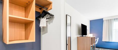 A hotel room with a wooden wardrobe, a mirror, a television, and a desk.