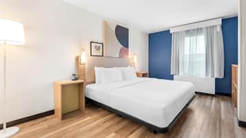 A modern hotel room with a large bed, bedside tables, a desk, and a window with curtains.