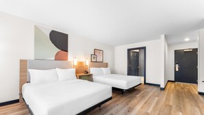 A hotel room with two beds, wooden flooring, a large abstract painting, and a door with a dark frame.