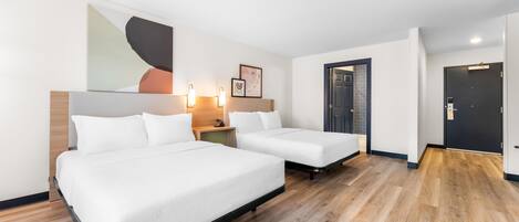 A hotel room with two beds, wooden flooring, a large abstract painting, and a door with a dark frame.