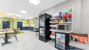A modern cafeteria with seating, a refrigerator, microwave, and vending machines.