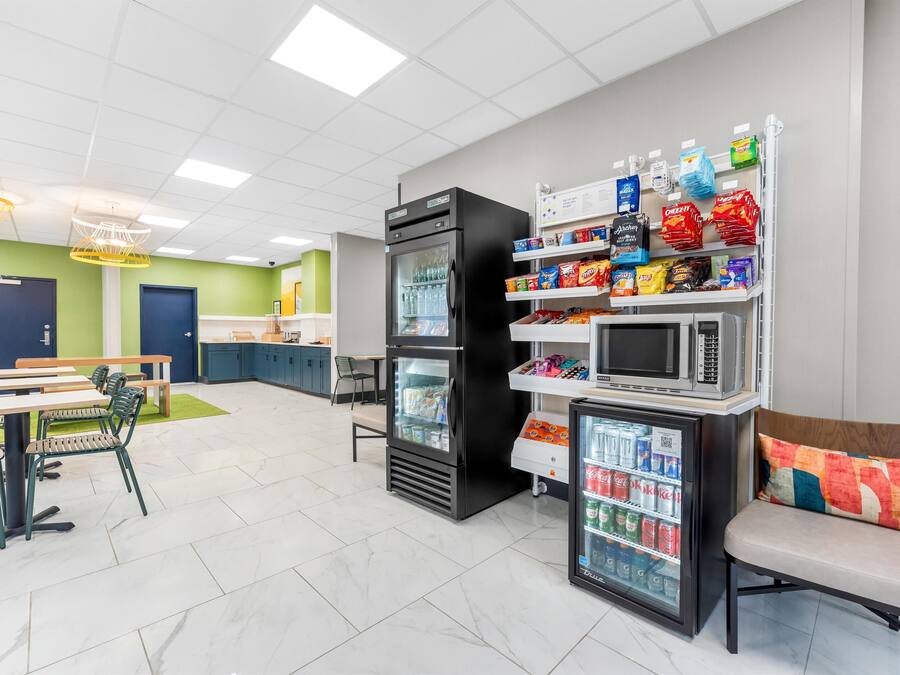 A modern cafeteria with seating, a refrigerator, microwave, and vending machines.