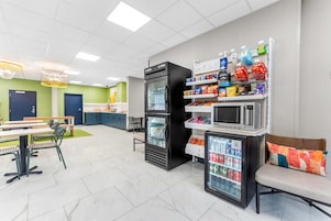Uma cafeteria moderna com mesas, geladeira, micro-ondas e máquinas de venda automática.