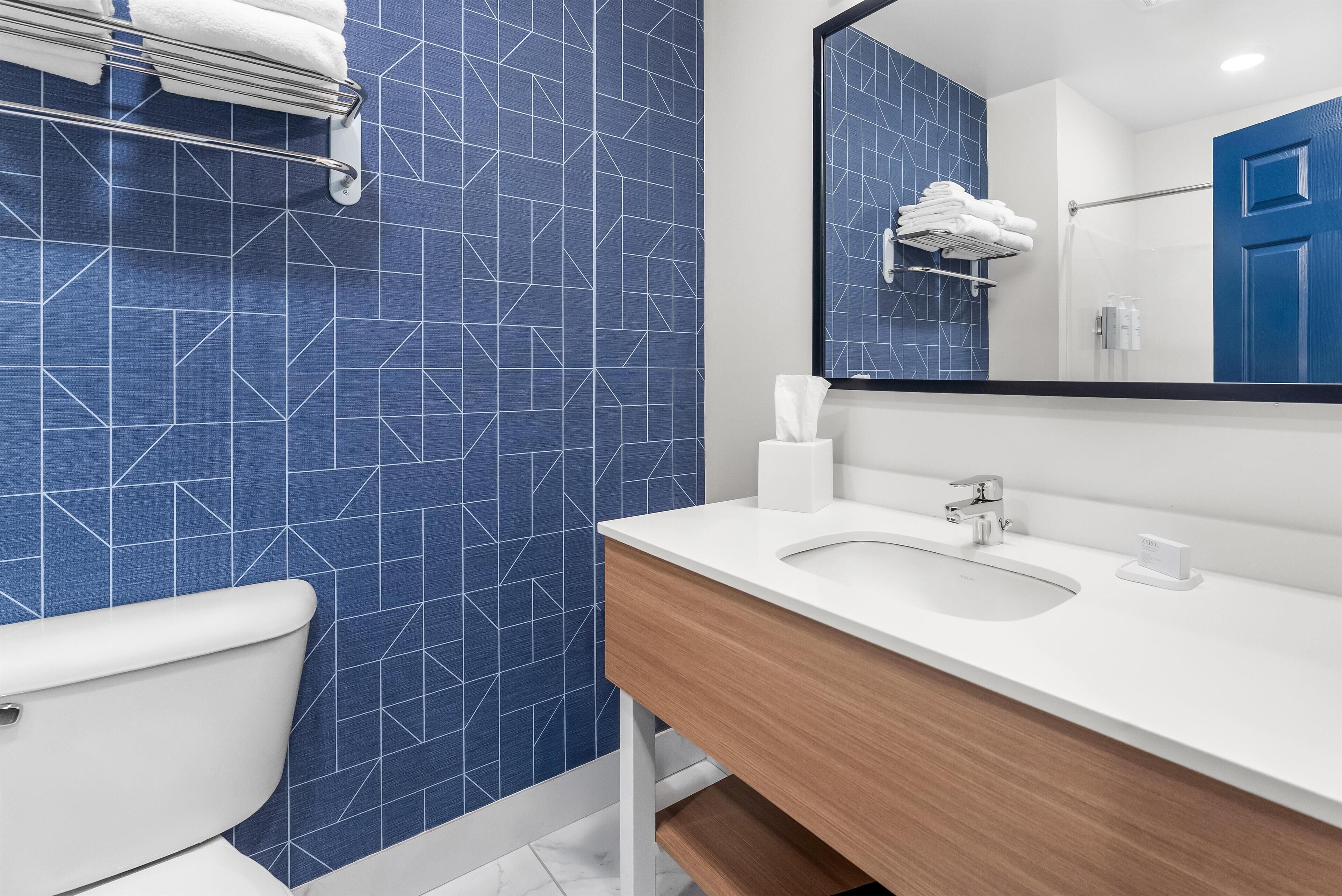 A modern bathroom with a blue geometric tile backsplash, a white sink, and a wooden vanity.
