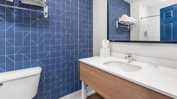 A modern bathroom with a blue geometric tile backsplash, a white sink, and a wooden vanity.