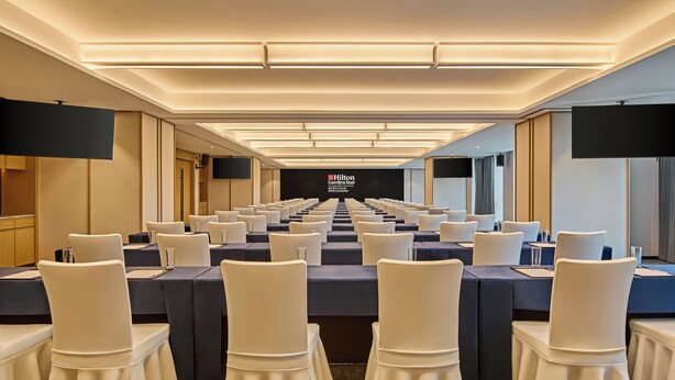 A conference room with rows of tables and chairs, a large screen at the front, and a sign reading "Hilton Conference Center." - Hilton Garden Inn Chongqing Yubei Central Park (Chongqing)