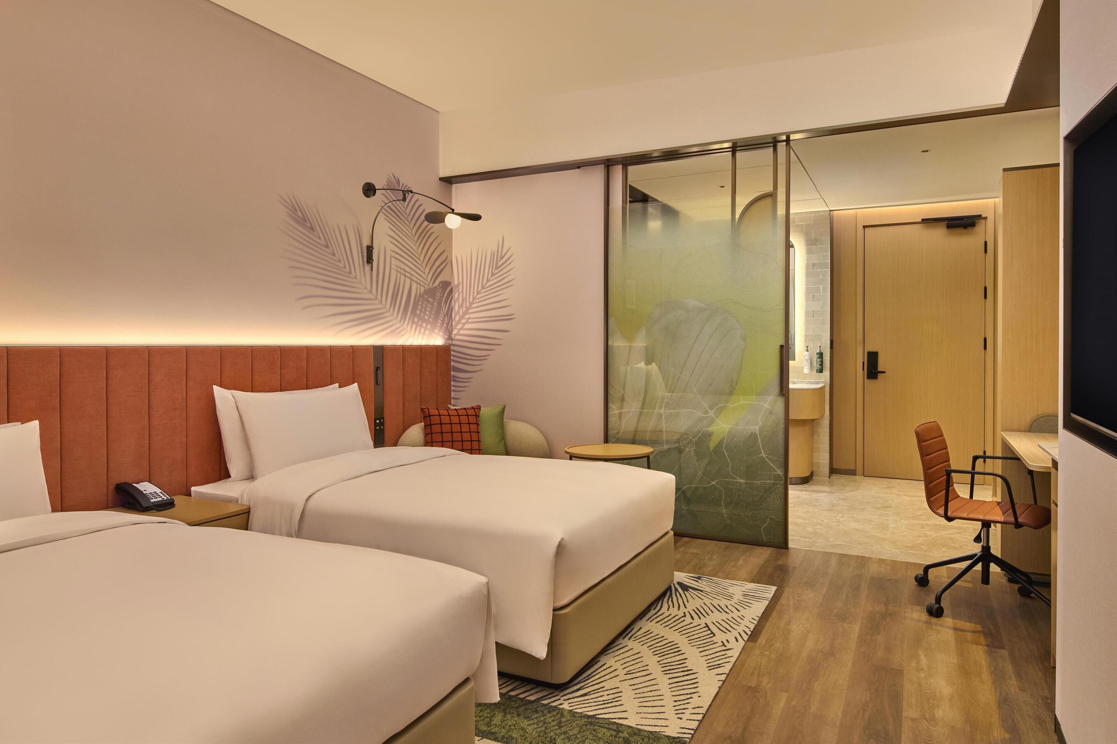Habitación de hotel con dos camas, un escritorio, una silla, un teléfono y una lámpara fijada a la pared.