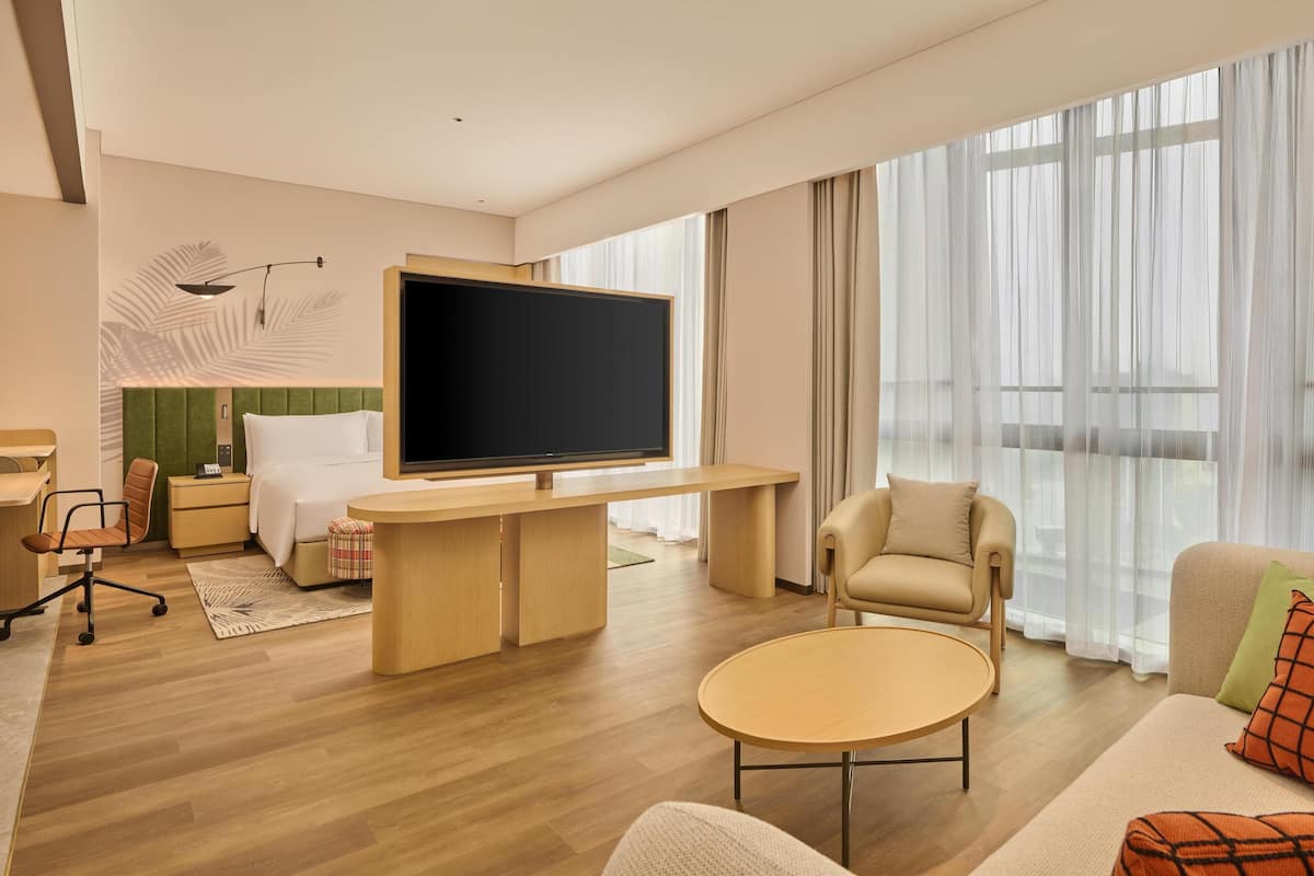 A modern hotel room with a large flat-screen TV, a comfortable sofa, a small round table, and a desk with a chair.