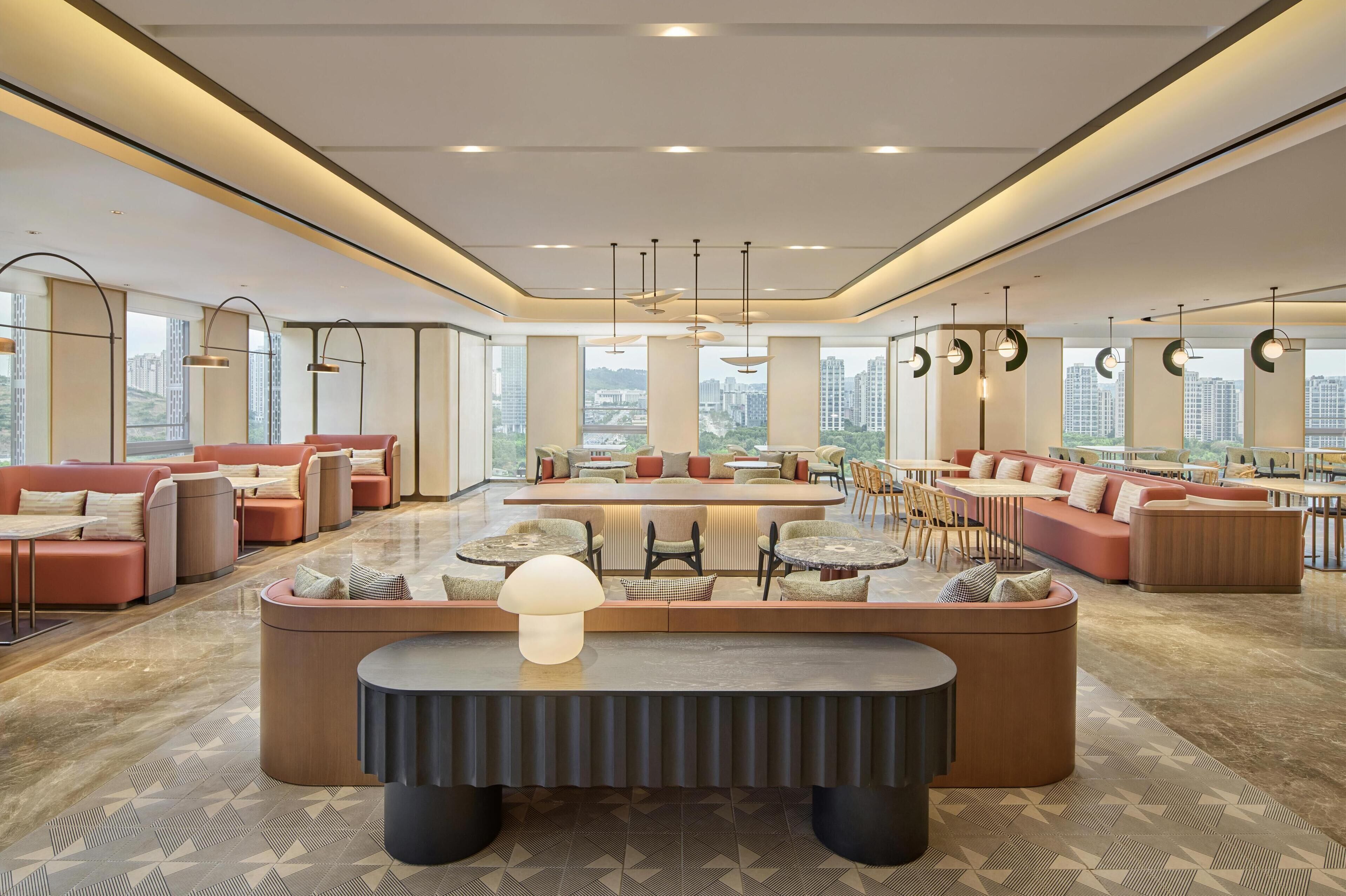 A spacious lobby with seating areas, a central coffee table, and large windows offering city views.