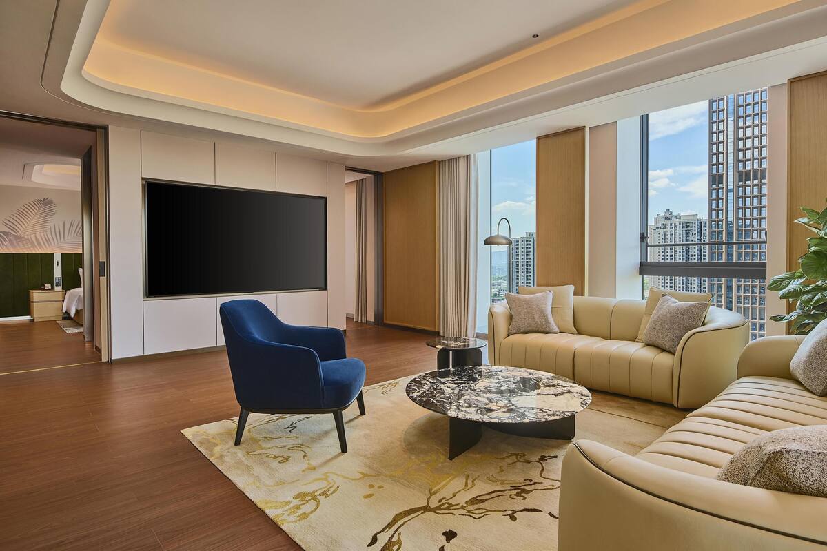 A modern living room with a large flat-screen TV, a blue armchair, a beige sofa, and a coffee table.