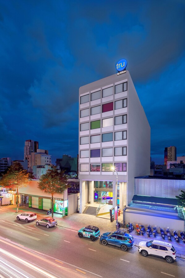 Un moderno edificio de hotel con un llamativo letrero de 'tru by Hilton', que presenta una fachada distintiva con bloques de ventanas coloridos y un techo plano.