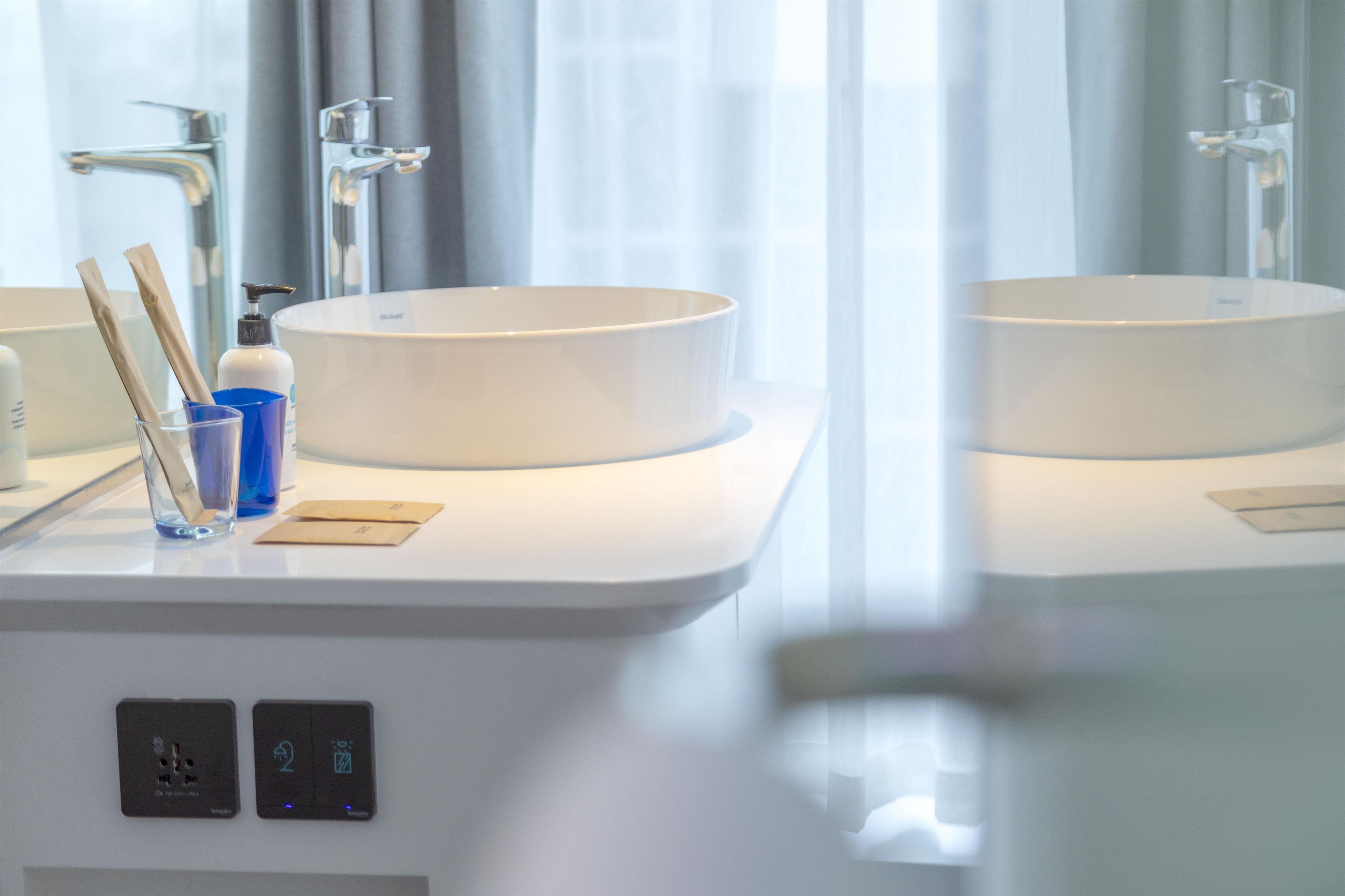 A modern bathroom with two sinks, a mirror, and a window with curtains.