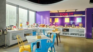 A breakfast area with purple walls, a counter with food items, and blue and yellow chairs. - Tru By Hilton Da Nang City Centre (Da Nang)