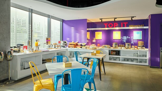 A breakfast area with purple walls, a counter with food items, and blue and yellow chairs. - Tru By Hilton Da Nang City Centre (Da Nang)
