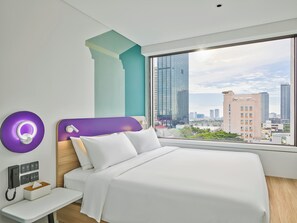 A modern hotel room with a large bed, a bedside table with a phone and tissues, a purple accent wall, and a city view through a large window. - Tru By Hilton Da Nang City Centre (Da Nang)