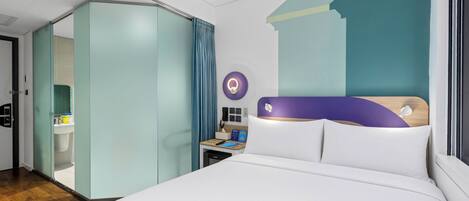 Ein modernes Hotelzimmer mit einem großen Bett, einem Kleiderschrank, einem Nachttisch mit Lampe und einem durch eine Glaswand abgetrennten Badezimmer.