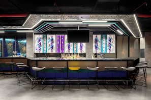 A bar area with a modern design, featuring a counter with stools and shelves of bottles.