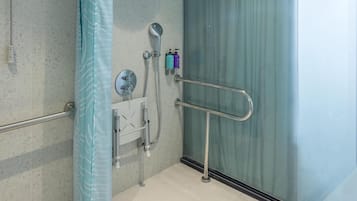 A modern shower area with a glass partition, a handheld showerhead, a wall-mounted faucet, and a handrail.