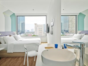 Una habitación de hotel moderna con dos camas, un amplio ventanal con vistas a la ciudad, un lavabo blanco y una silla.