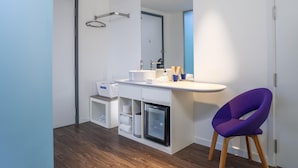 A modern bathroom with a white vanity, a small refrigerator, a purple chair, and a towel rack. - Tru By Hilton Da Nang City Centre (Da Nang)