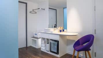 Un baño moderno con tocador blanco, un refrigerador pequeño, una silla morada y un perchero.