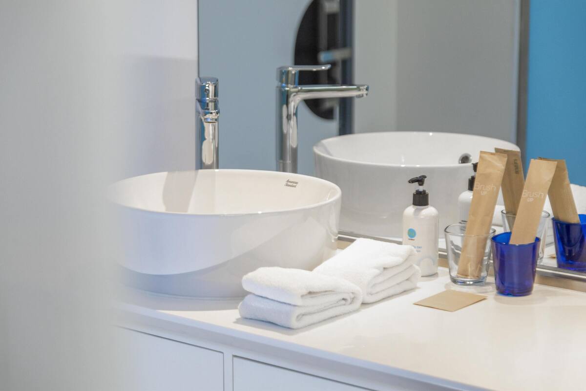 Un baño moderno con un lavamanos grande de color blanco, un espejo y un recipiente de vidrio azul con cepillos de dientes.