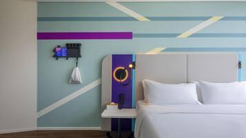 A hotel room with a bed, a bedside table with a lamp, a wall-mounted phone, and a small table with a tissue box.