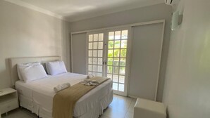A bedroom with a bed, a nightstand, a bench, and a sliding glass door to a balcony. - Duplex with barbecue 70 meters from the sea on Ingleses beach (Ingleses Sul Florianópolis)