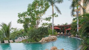 Un área de piscina con sillas de descanso, una pérgola y vegetación tropical.