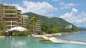 Un resort con piscina, acceso a la playa y montañas al fondo.
