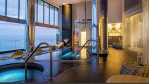 Un área interior de piscina moderna con vista al océano, un jacuzzi y una zona de estar con pared de vidrio.