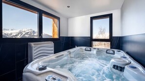 A modern bathroom with a hot tub, large windows, and a view of snow-capped mountains.