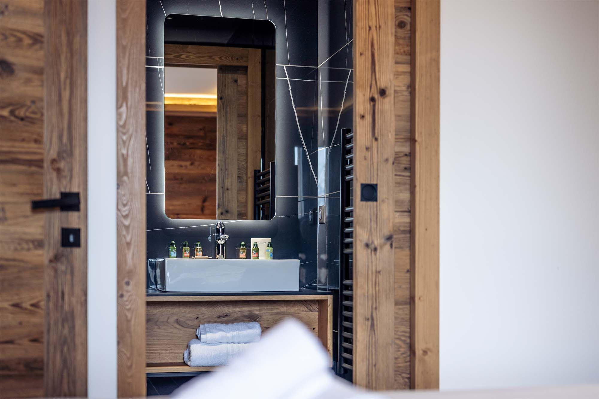 Une salle de bain avec une porte en bois, un miroir, un lavabo et un porte-serviettes.
