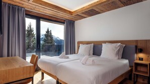 Ein Hotelzimmer mit zwei Betten, Holzbalkendecke, einem Balkon mit Bergblick und einem kleinen Tisch.