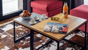 Ein gemütlicher Sitzbereich mit Tisch, gedeckt für das Frühstück, inklusive Croissants, Kaffeetassen und einer Saftflasche.