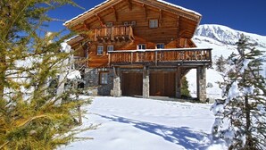 Un chalet en bois doté d’un balcon, avec des fondations en pierre et une vue sur une montagne enneigée.