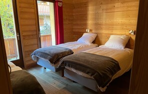 Habitación de cabaña de madera con dos camas, puerta corrediza de vidrio al exterior y una cortina roja.
