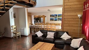 Un salon comprenant une table basse en bois, un canapé en cuir noir et un coin repas avec des chaises et une table en bois.