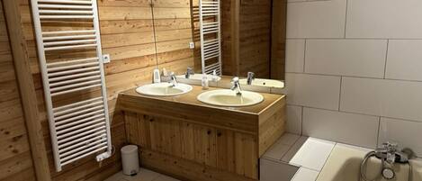 A wooden-paneled bathroom with two sinks, a mirror, and a bathtub.