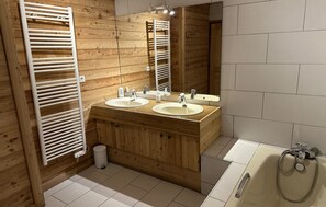Un baño con paneles de madera, dos lavamanos, un espejo y una bañera.