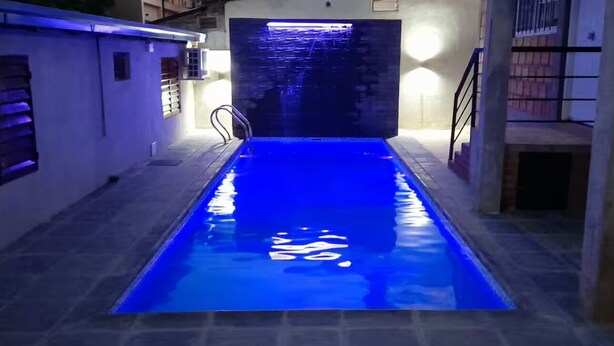 Una piscina con iluminación azul, suelo de baldosas y una pared con ventana y lámpara.