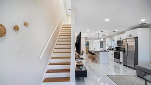 A modern kitchen with a central island, stainless steel appliances, and a staircase leading to another level.