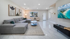 A modern living room with a grey sectional sofa, a round coffee table, and a flat-screen TV on the wall.