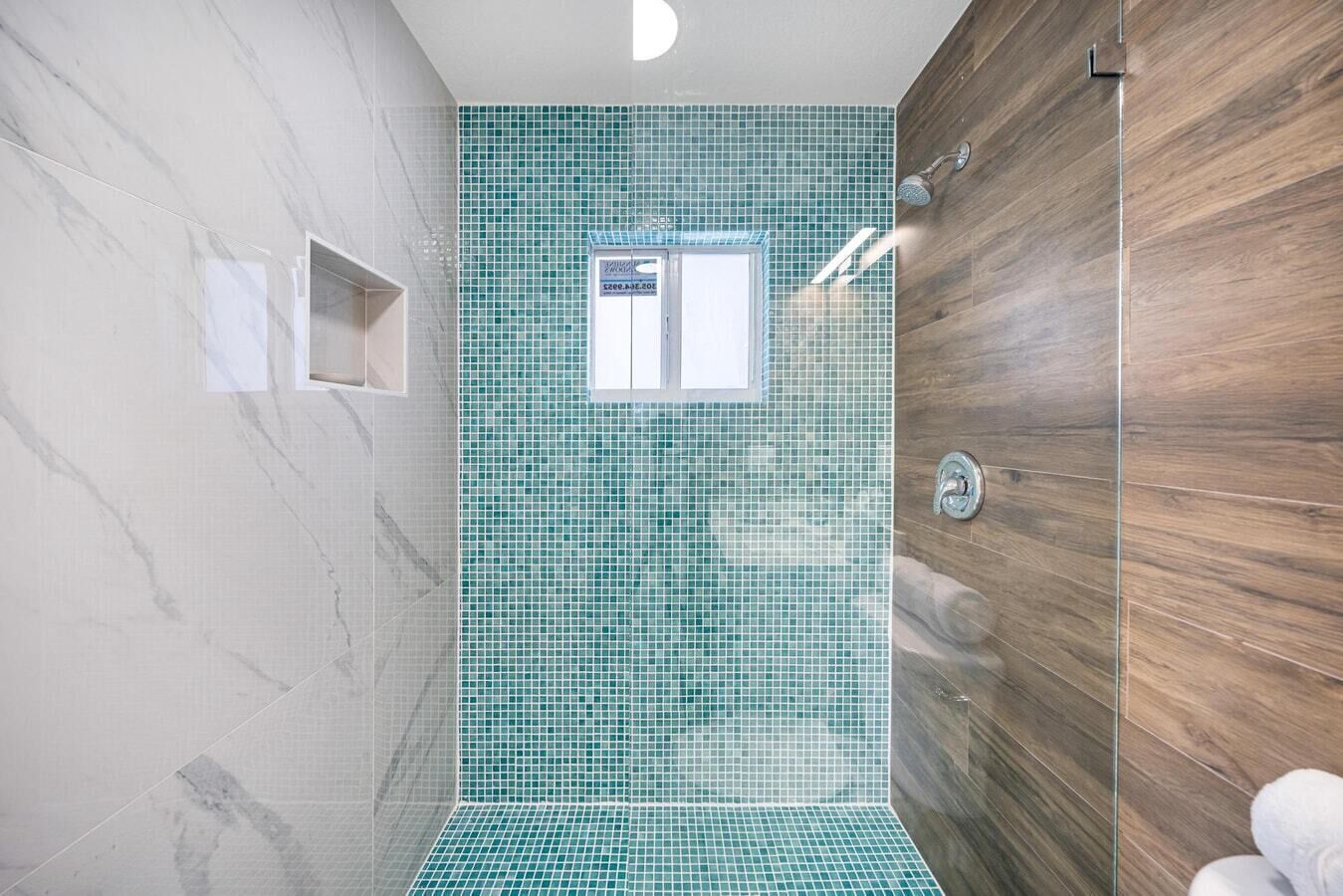 A modern shower area with a glass door, a tiled wall, and a wooden panel.
