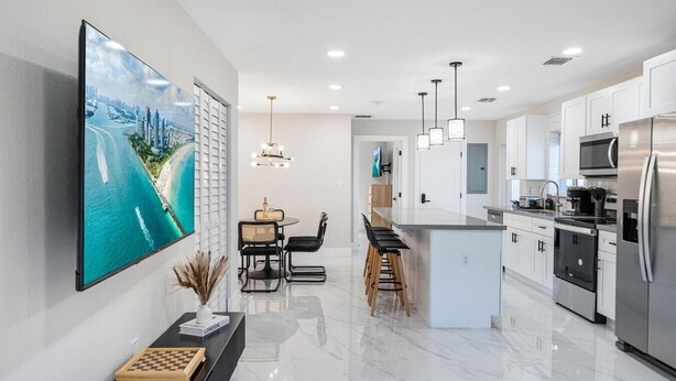 A modern kitchen with a large island, stainless steel appliances, and a dining area with a view of a cityscape.