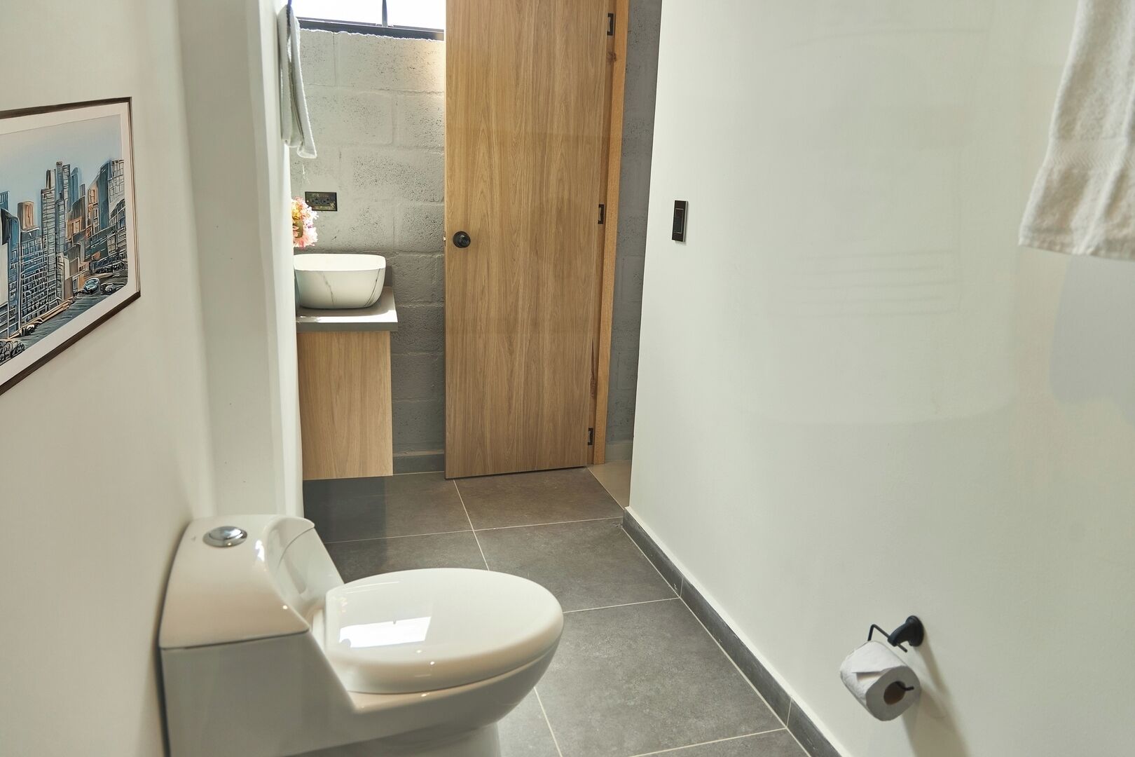 Une salle de bain moderne équipée de toilettes, d’un lavabo et d’une porte en bois donnant accès à une zone douche.