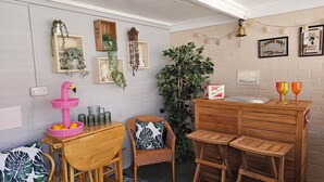 Une pièce chaleureuse avec une table en bois, des chaises en osier, une plante en pot et une boîte de rhum Bacardi.
