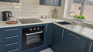 Une cuisine moderne avec des armoires bleues, une cuisinière noire, un plan de travail blanc et une fenêtre donnant sur un bâtiment en briques.