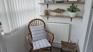 Une chaise en osier avec des coussins à rayures, une petite table d’appoint en osier et un radiateur blanc.